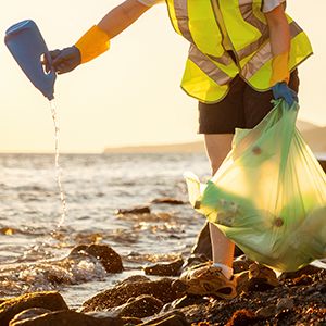 Person in yellow vest picking up plastic trash at beach